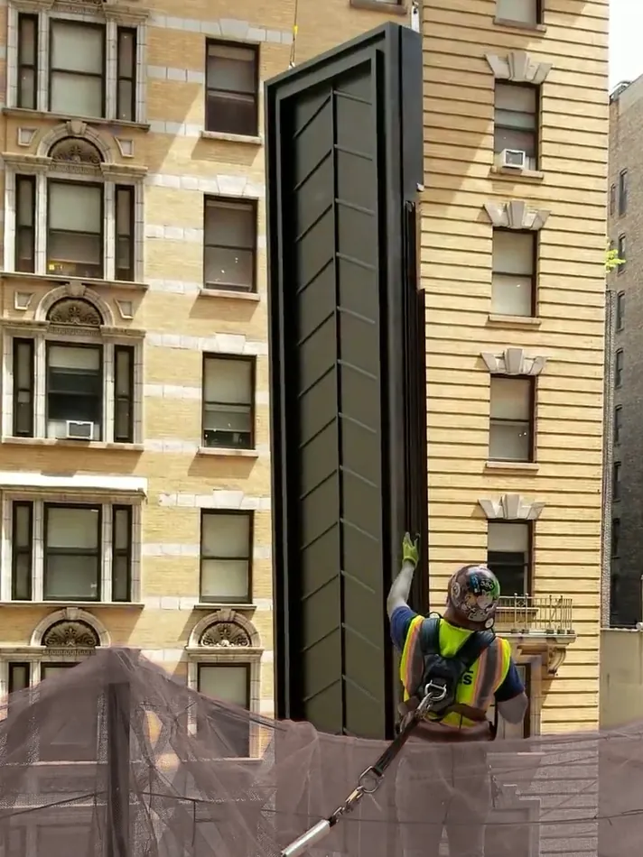 Ironworker guiding a steel panel into place against a pre-war Manhattan apartment facade