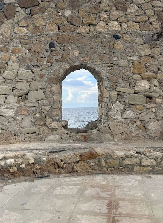 Window cut into an old stone wall framing the sea